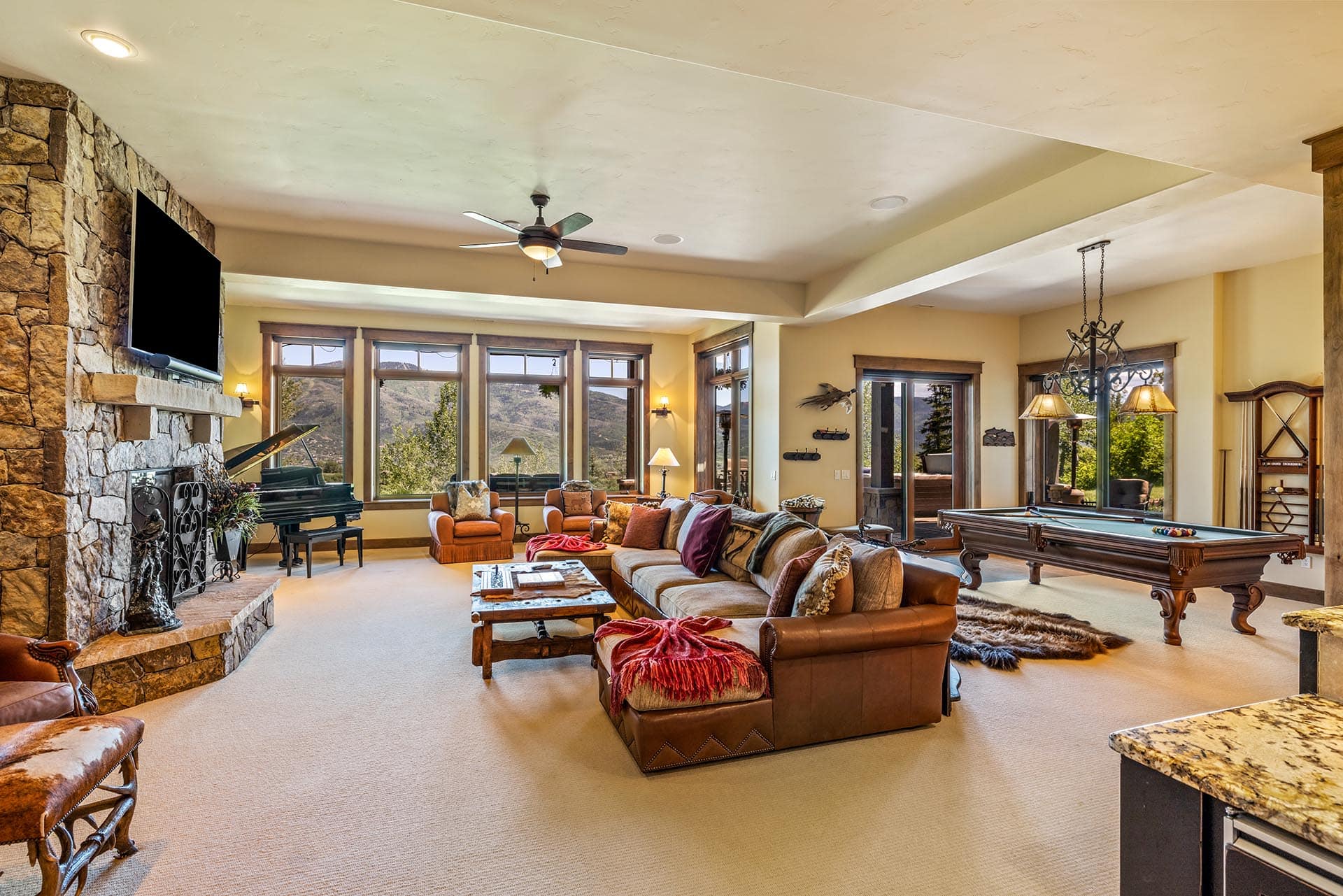 Spacious living room with a stone fireplace, wall-mounted TV, and large windows showing a mountain view.