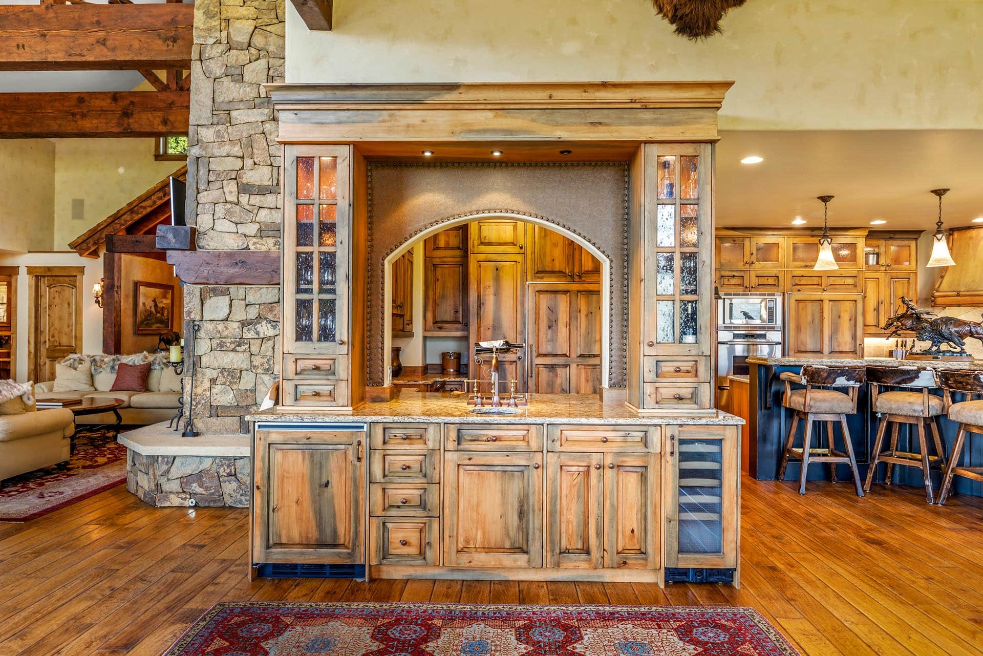 Rustic kitchen with a large wooden island, stone pillar, and warm, cabin-style cabinetry and seating area.