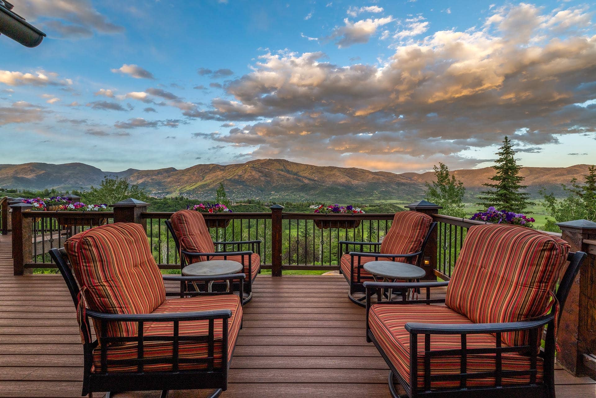 Patio deck with striped cushioned chairs and small tables, overlooking a valley and distant mountains under a blue sky.