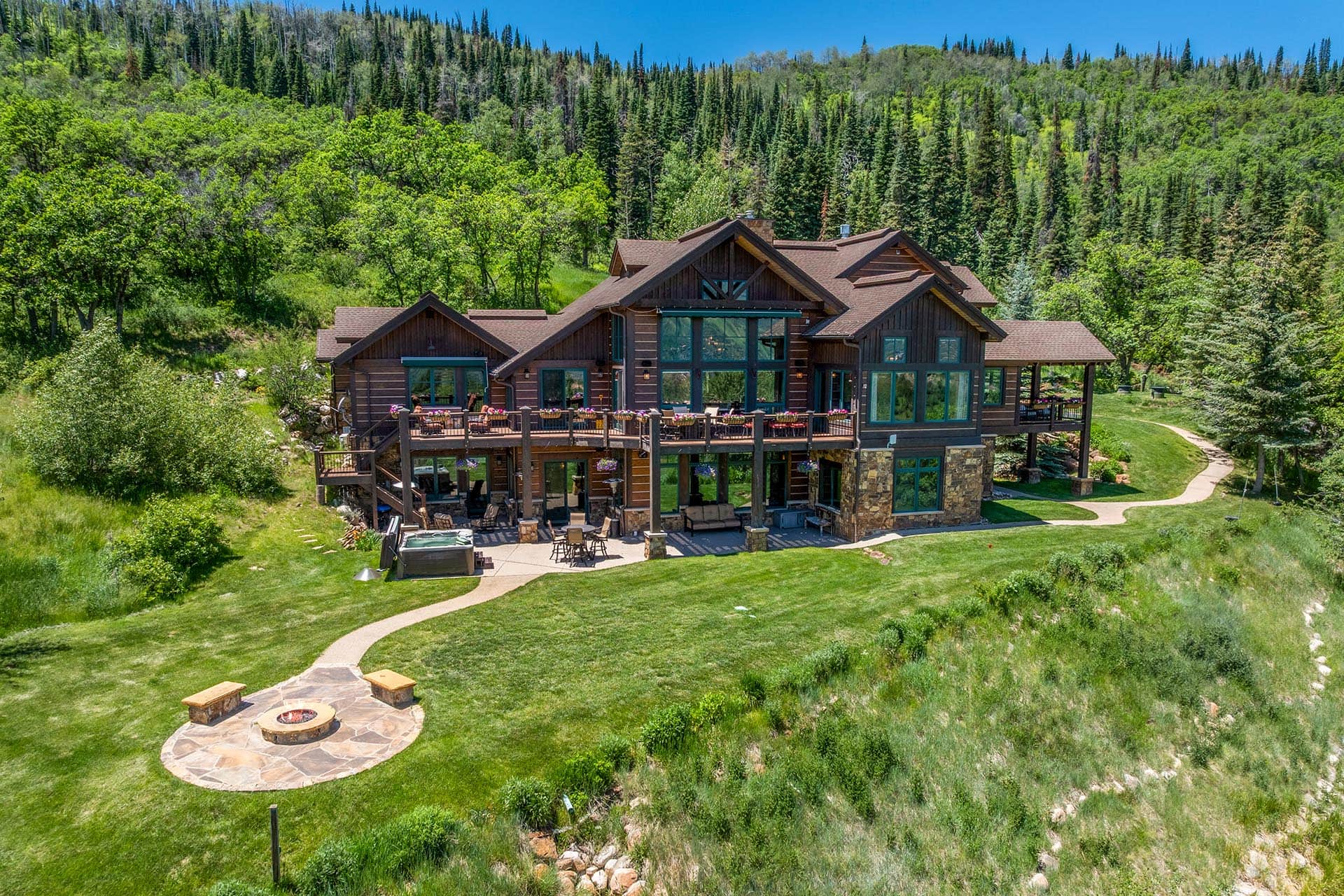 Rustic wooden lodge with a large deck and outdoor seating, set among green trees on a hillside.