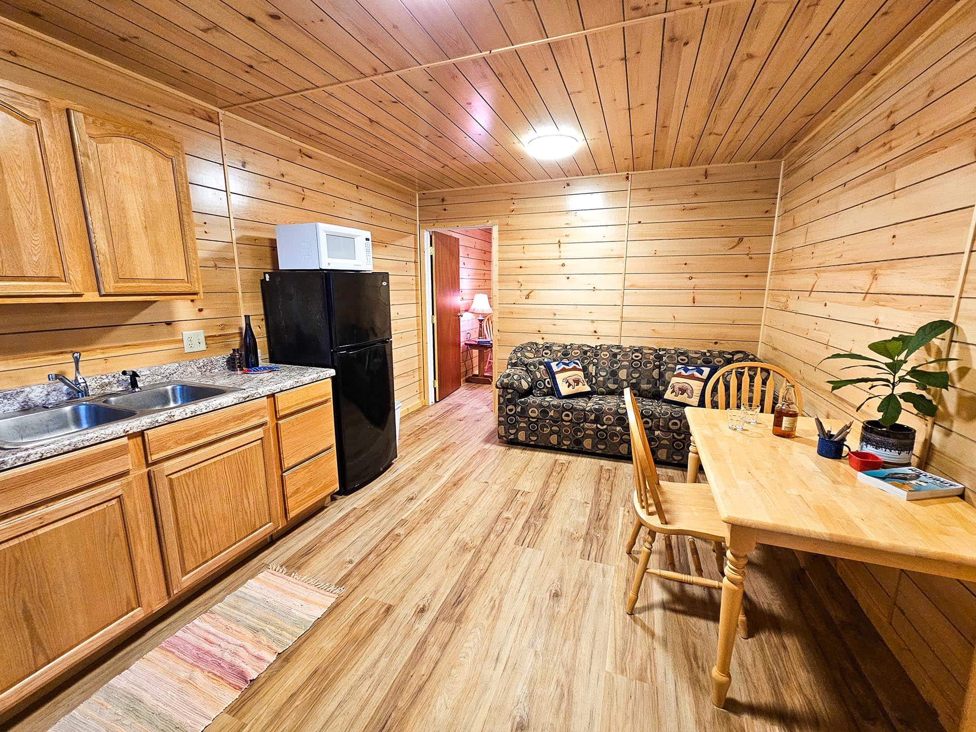 Wood-paneled cabin kitchen and living area with a black refrigerator, microwave, sink, and a patterned sofa nearby.