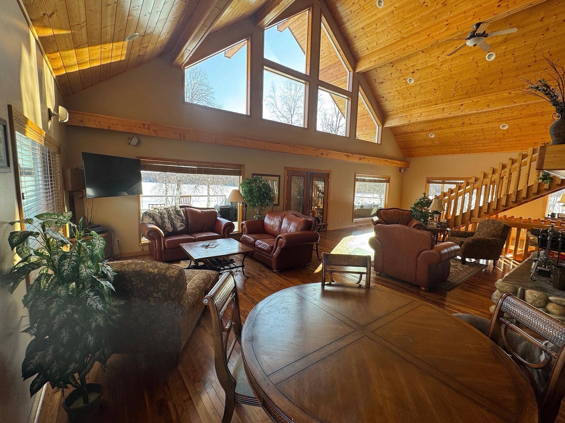 Spacious lounge with a vaulted wood ceiling, large window walls, and leather sofa set around a wooden coffee table.