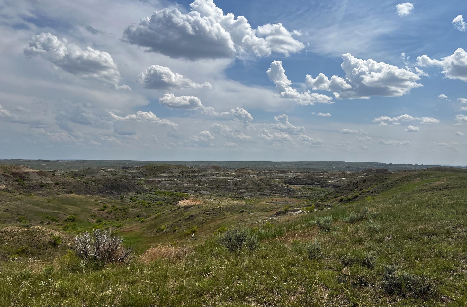 Wide arid landscape with rolling brown hills, sparse green vegetation, and a cloudy blue sky above the horizon.