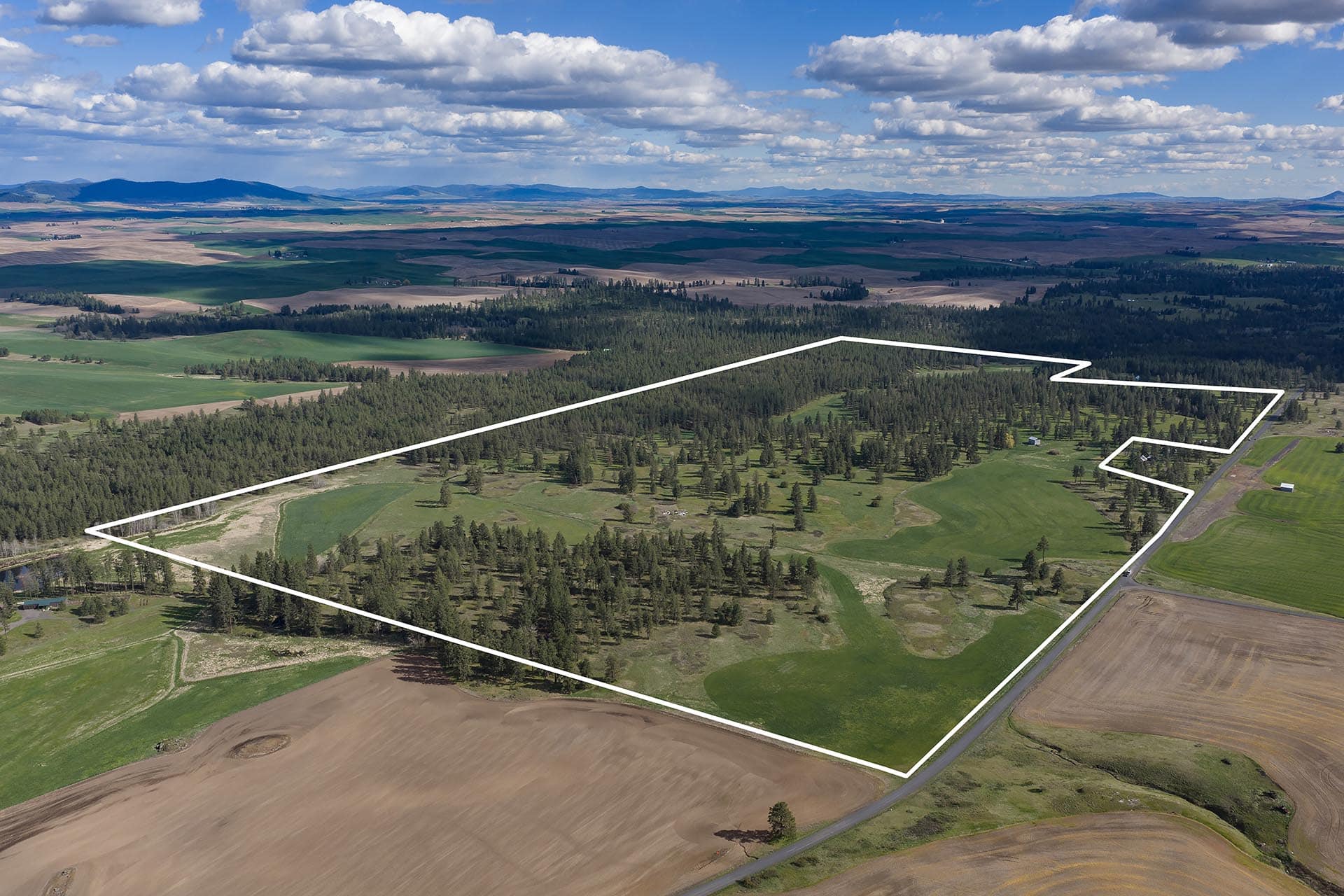 Aerial view of a large rural property outlined by white boundary lines over fields and forested areas.