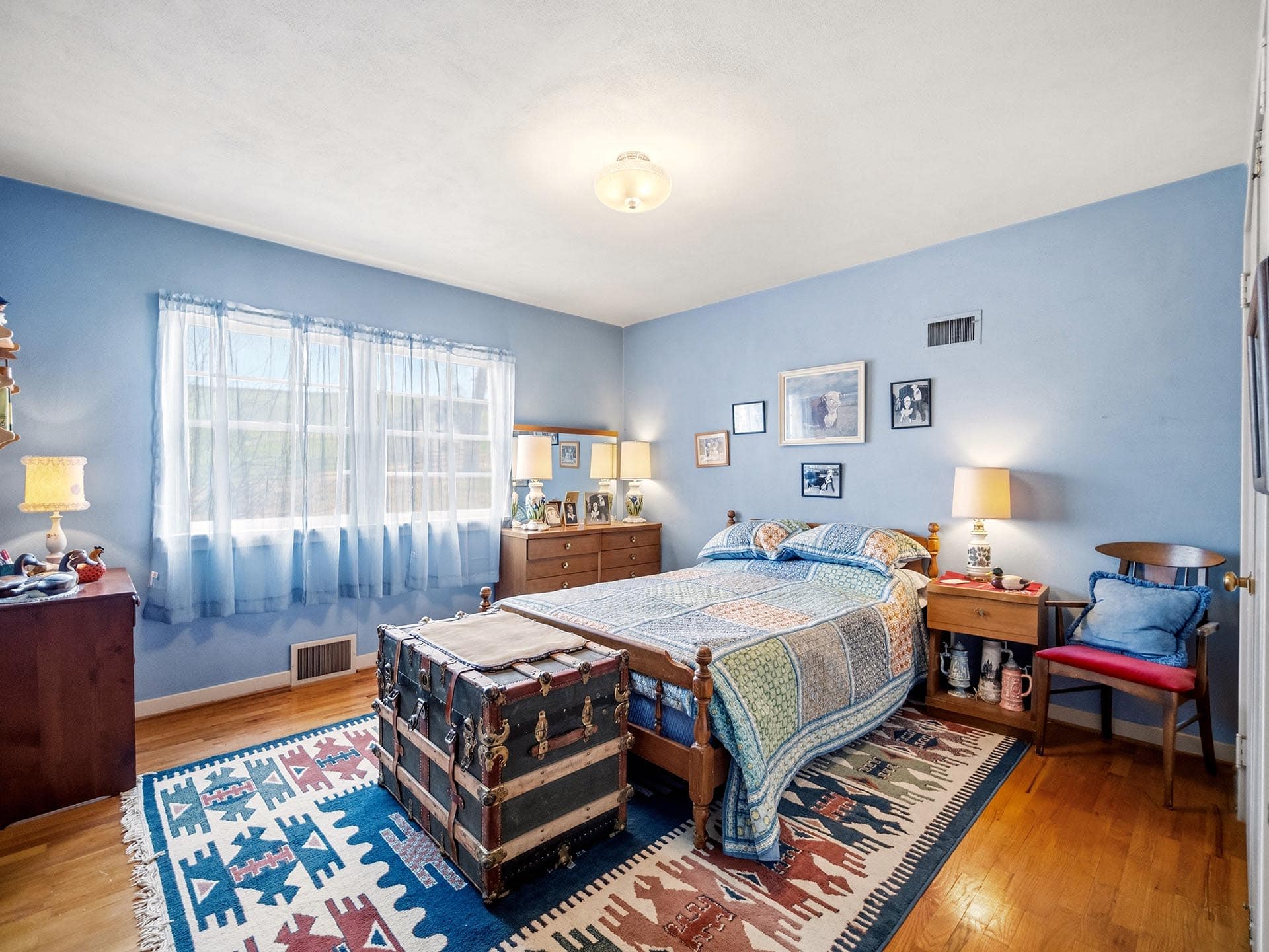 Blue bedroom with a single wooden bed, quilted blue bedding, a large vintage trunk at the foot, and a colorful geometric rug on a wooden floor.
