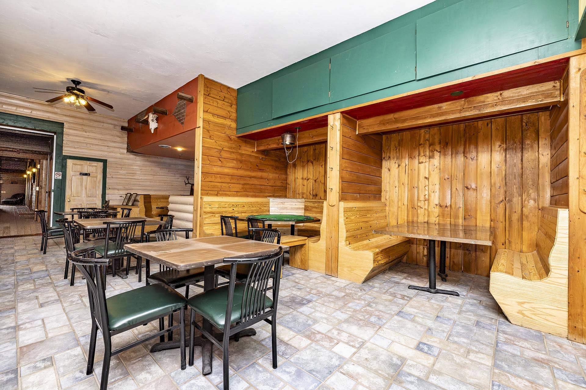 Indoor rustic cafe seating with wooden tables and black chairs, wood-paneled walls, and teal cabinets overhead.