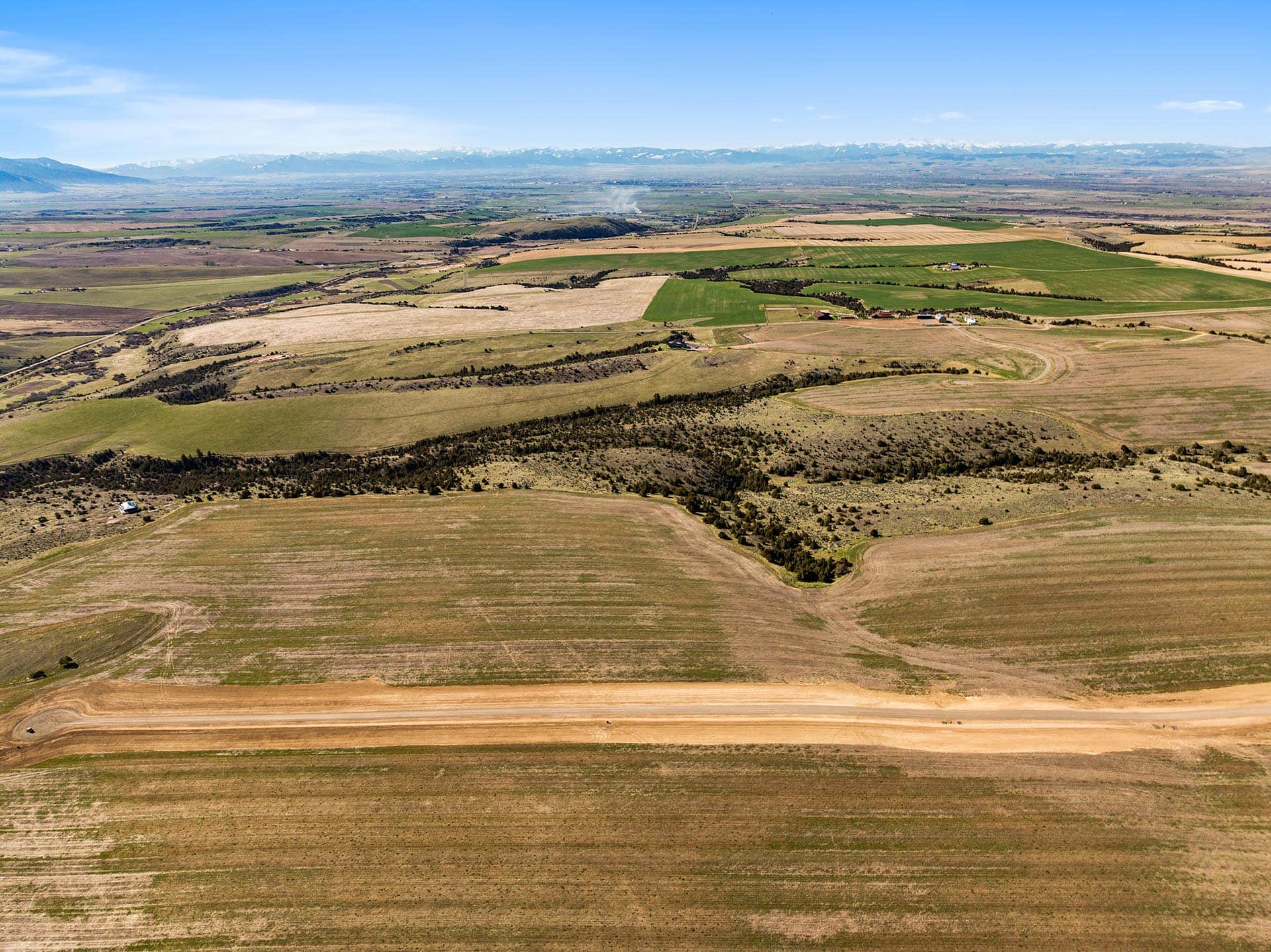 expansive farm fields with distant structures and mountain backdrop land for sale montana golden meadow at sxs ranch