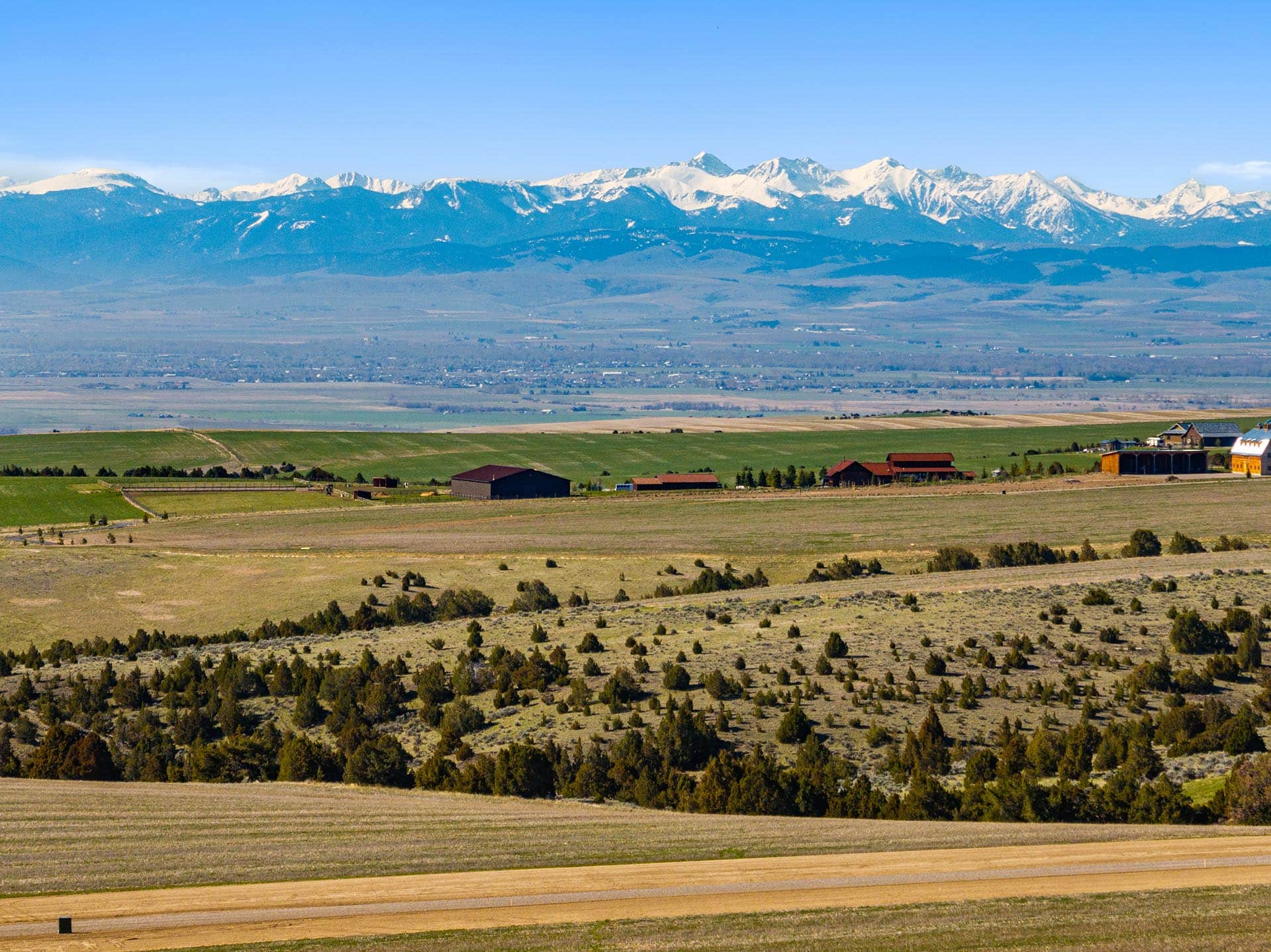 farm buildings with juniper trees and snow capped mountains land montana golden meadow at sxs ranch