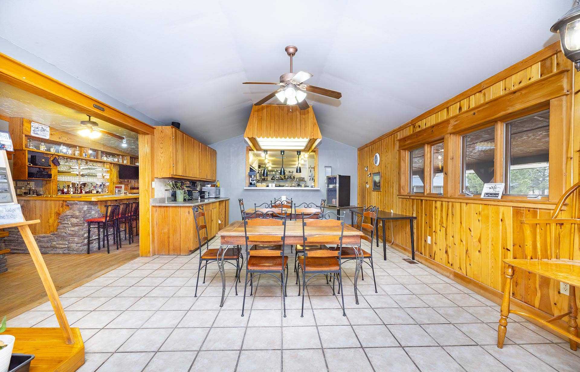 Rustic wood-paneled restaurant interior with a central ceiling fan and a dining area facing an open kitchen.",