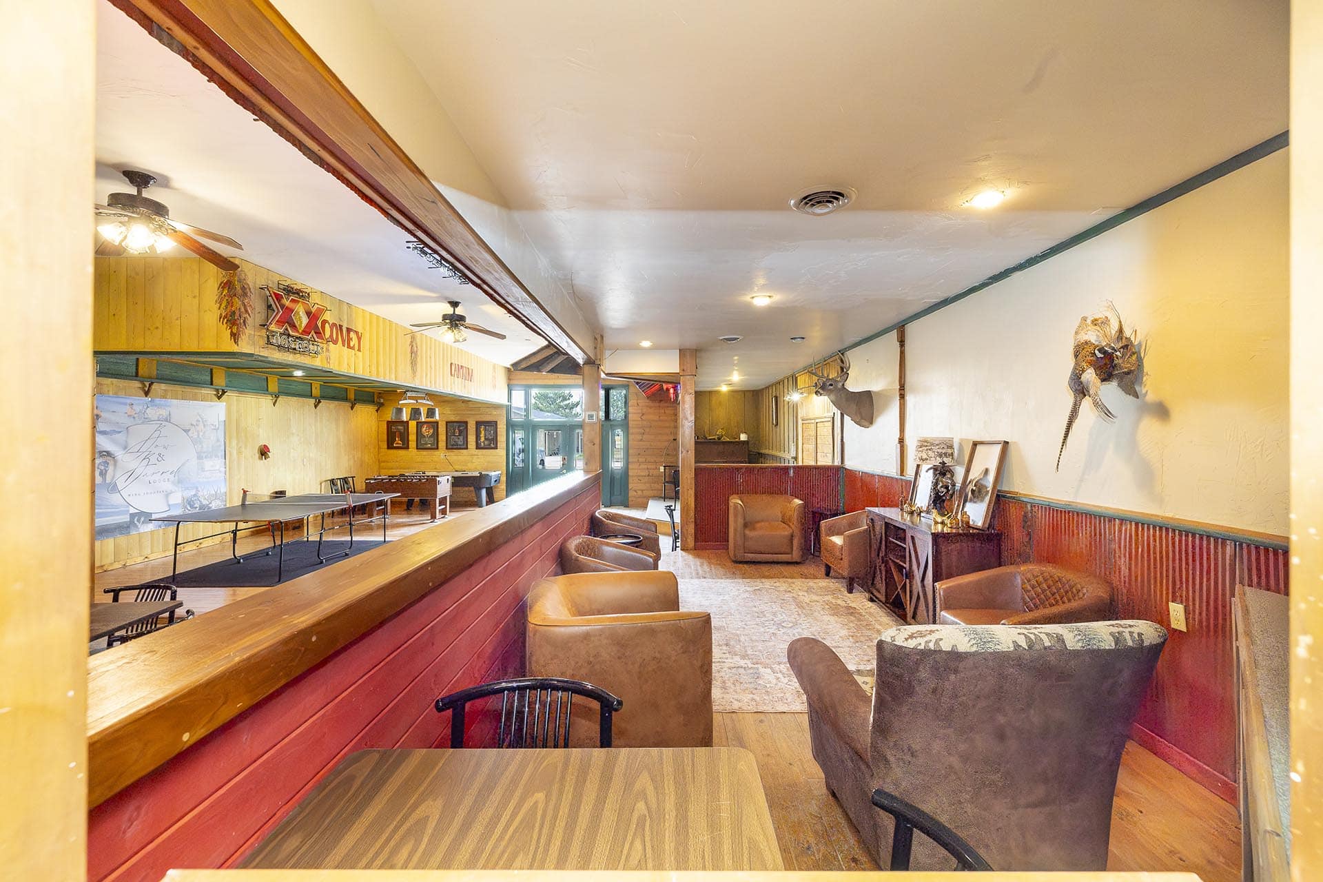 Wide shot of a cozy rustic pub interior with a long wooden bar and red paneling along the lower wall.