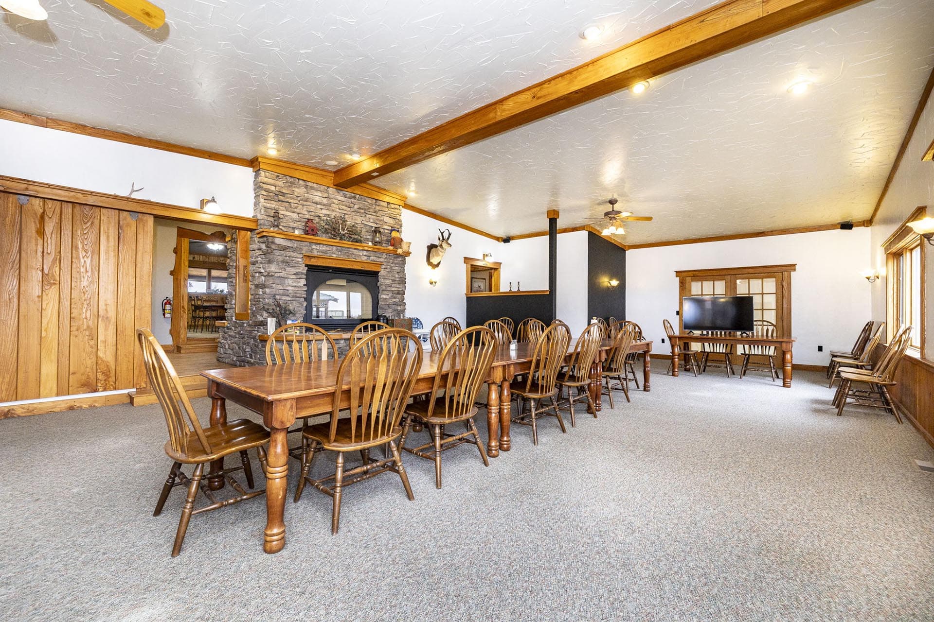 Rustic lodge-style conference room with a long wooden table, many chairs, and a stone fireplace centerpiece.
