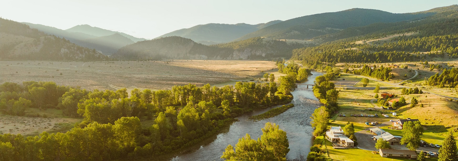Aerial view of a winding river through a green valley with trees, hills in the distance, and a small town along the shore.
