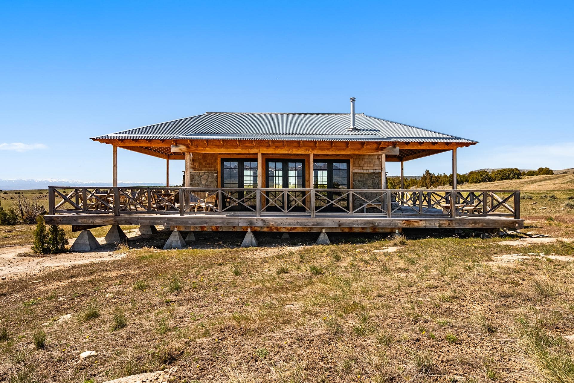 Wooden cabin on stilts with a wraparound deck in a dry grassland under a clear blue sky.**Caution**: remove the bold formatting in final usage