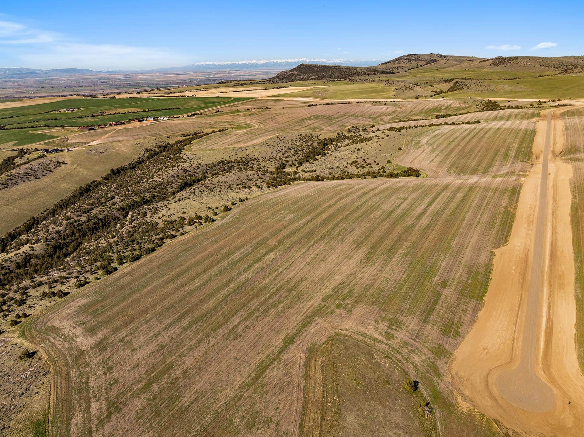 Aerial view of patchwork farmland with fields, rolling hills, and distant mountains under a blue sky.