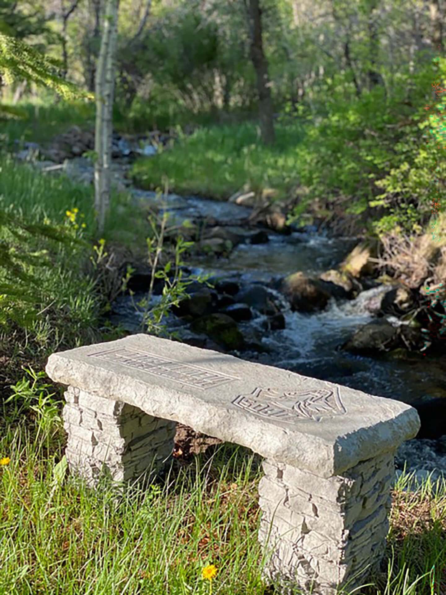 Stone bench with carved patterns beside a rocky forest stream.