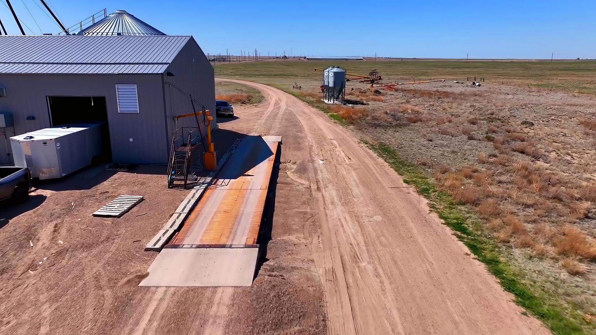 Industrial building with metal siding and loading ramp on a dirt farm road under a clear blue sky
