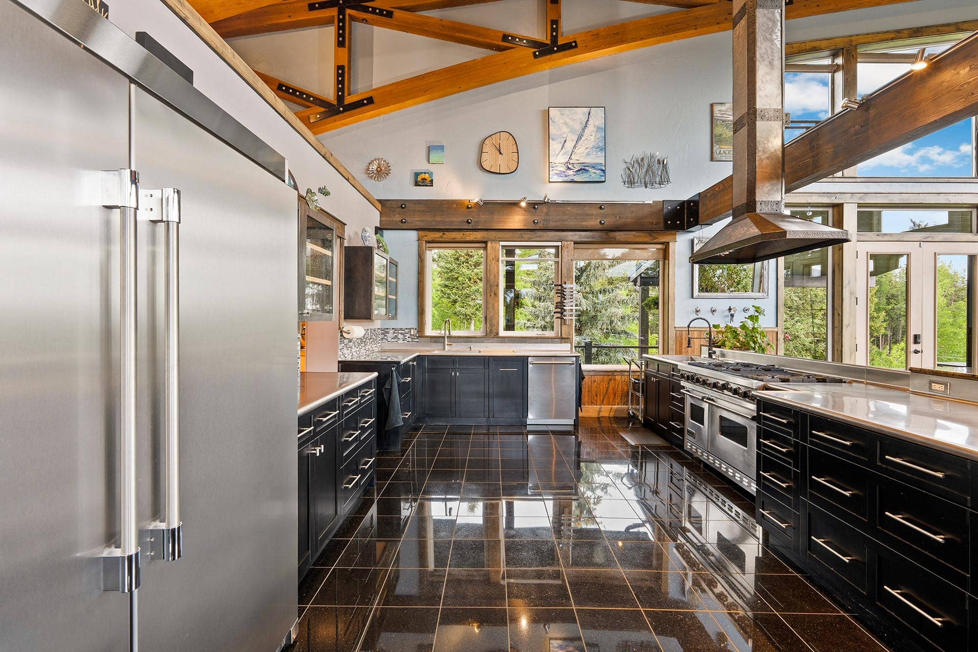Spacious contemporary kitchen with black cabinetry, stainless steel appliances, and a large range hood under exposed wooden beams.