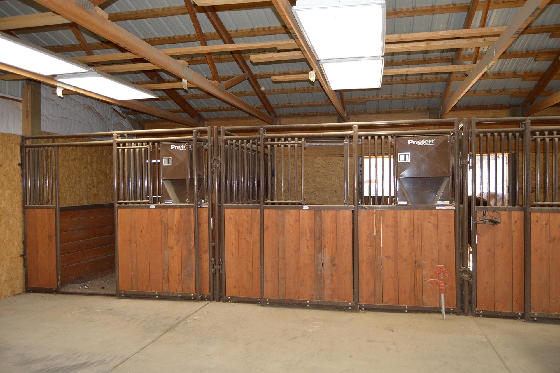 Interior of a horse stable with row of brown wooden stalls and metal bars under a wooden beam ceiling