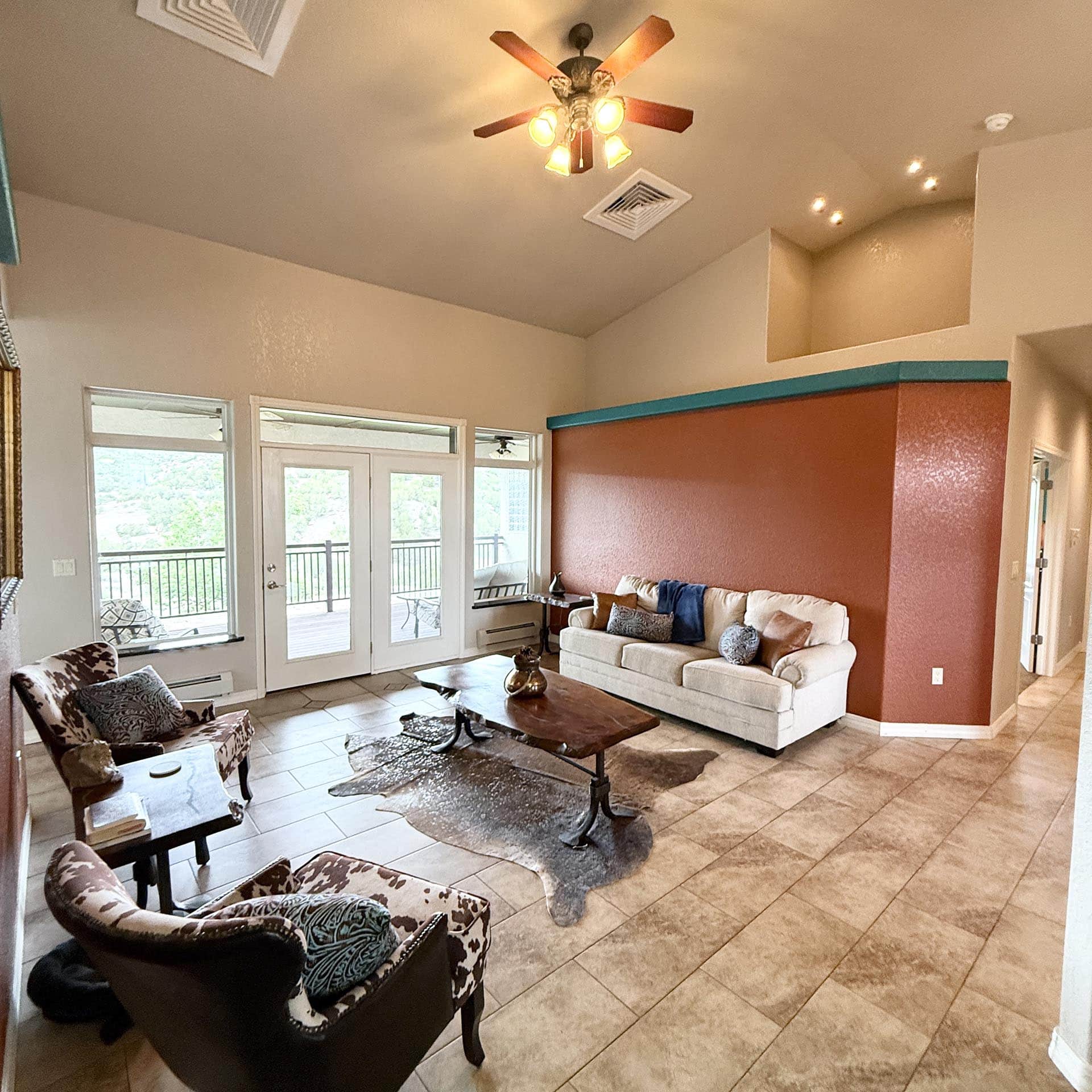 Open living room with white sofa, two patterned armchairs, and a wooden coffee table; glass doors open to a balcony.
