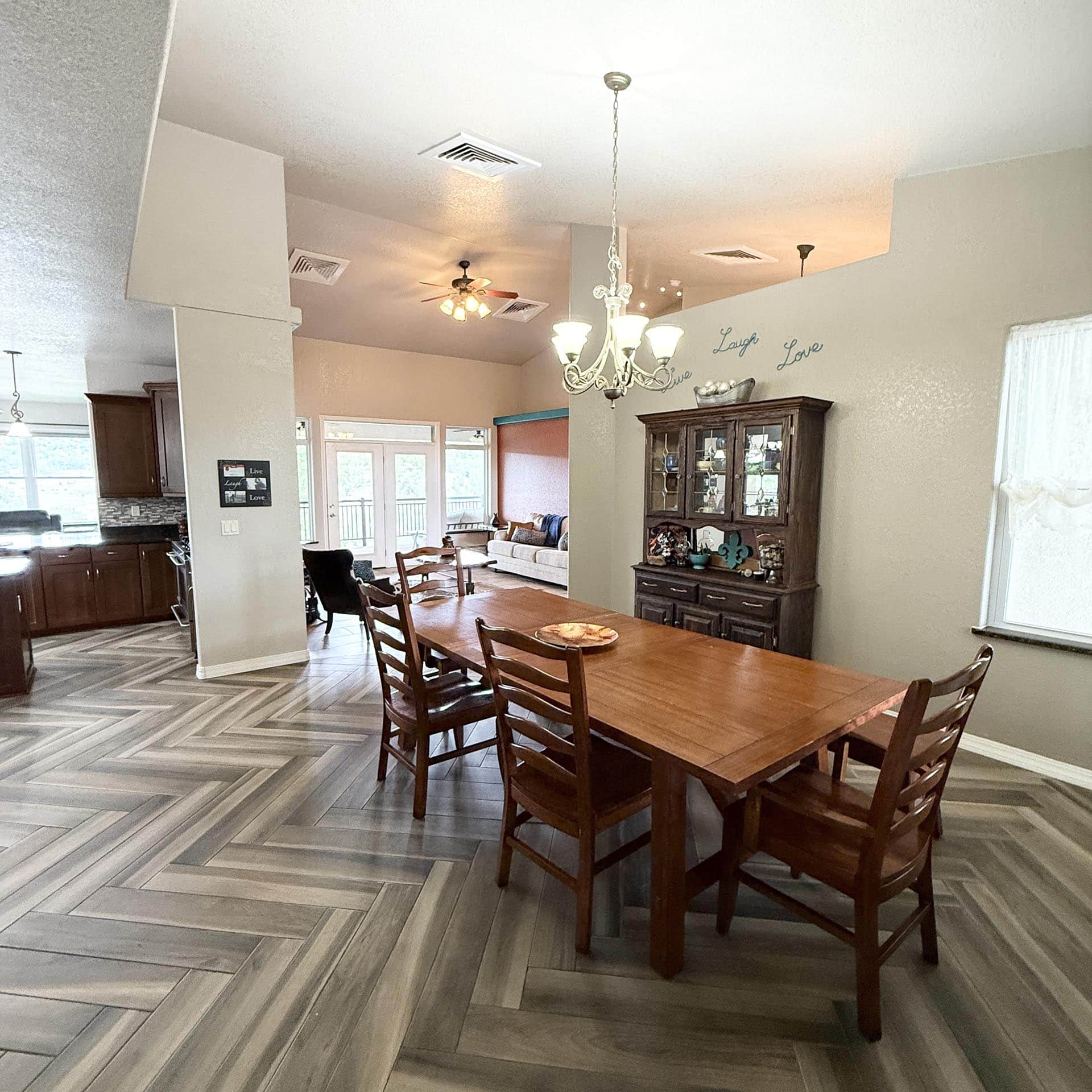 Dining room with a long wooden table and chairs, gray herringbone floor, and a chandelier overhead.