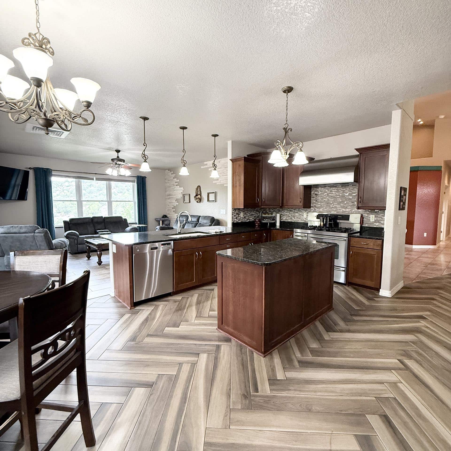 Open-concept kitchen with a large island, dark wood cabinets, and pendant lights in a bright living area.