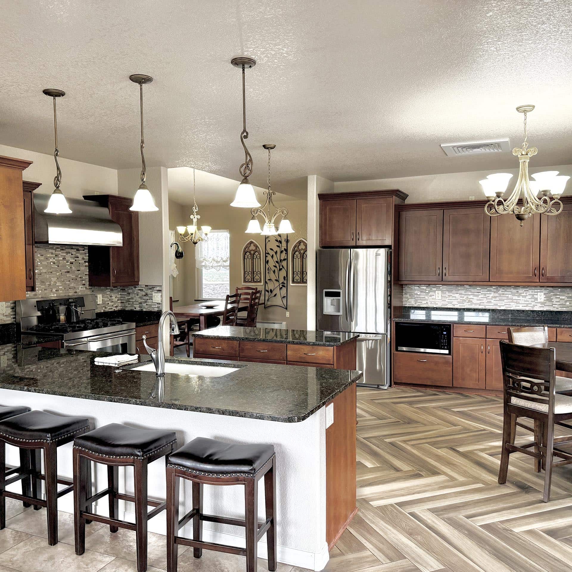 Modern kitchen with granite island, dark wood cabinets, and hanging pendant lights over the counter.