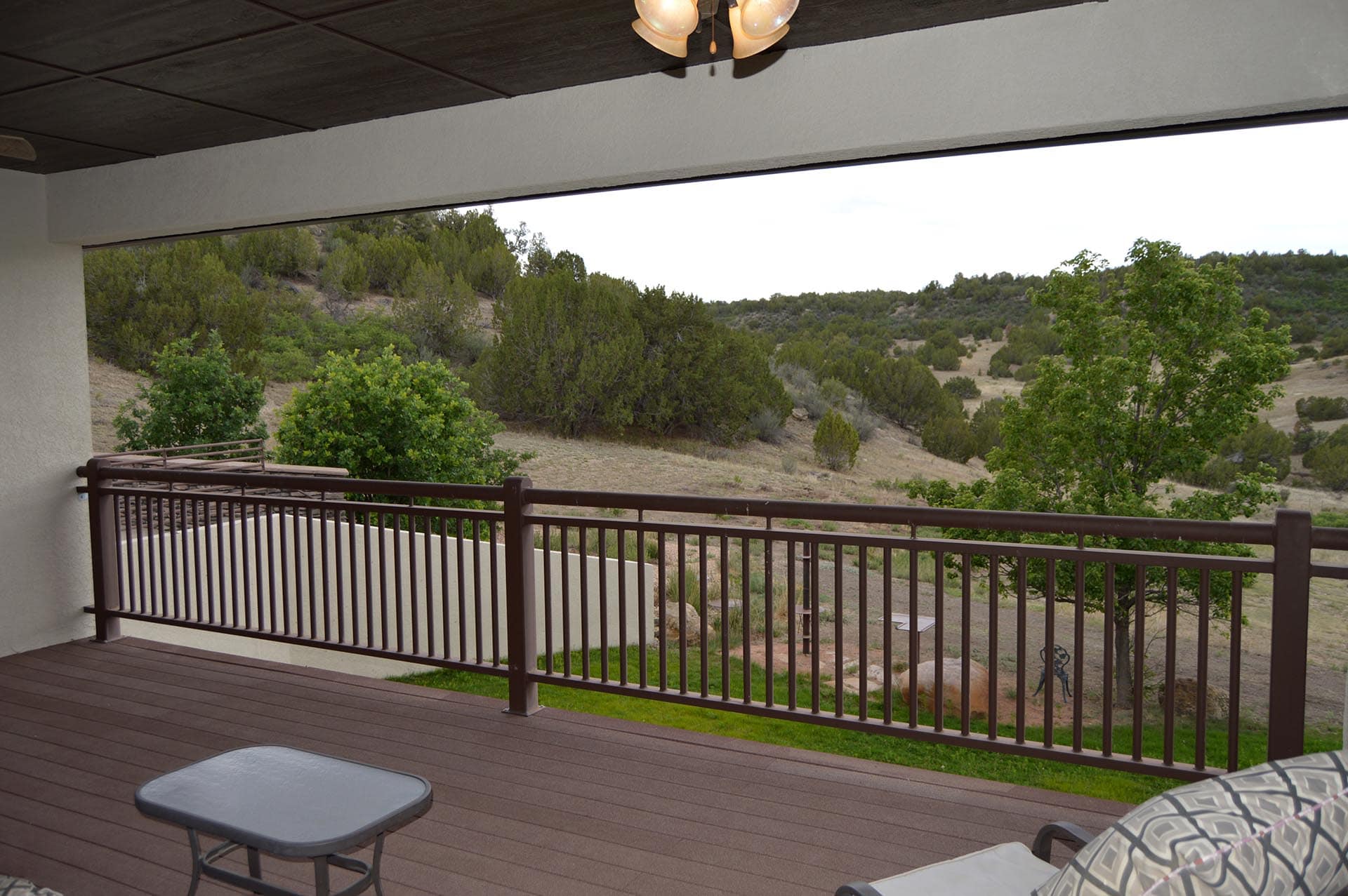 Balcony with brown railing overlooking a hillside dotted with trees and scrubby terrain.