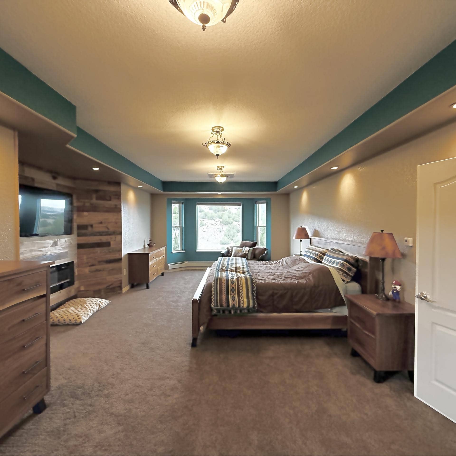 Two twin beds with matching brown quilts and patterned throws in a wood-accented bedroom with teal walls and ceiling lights at the center.