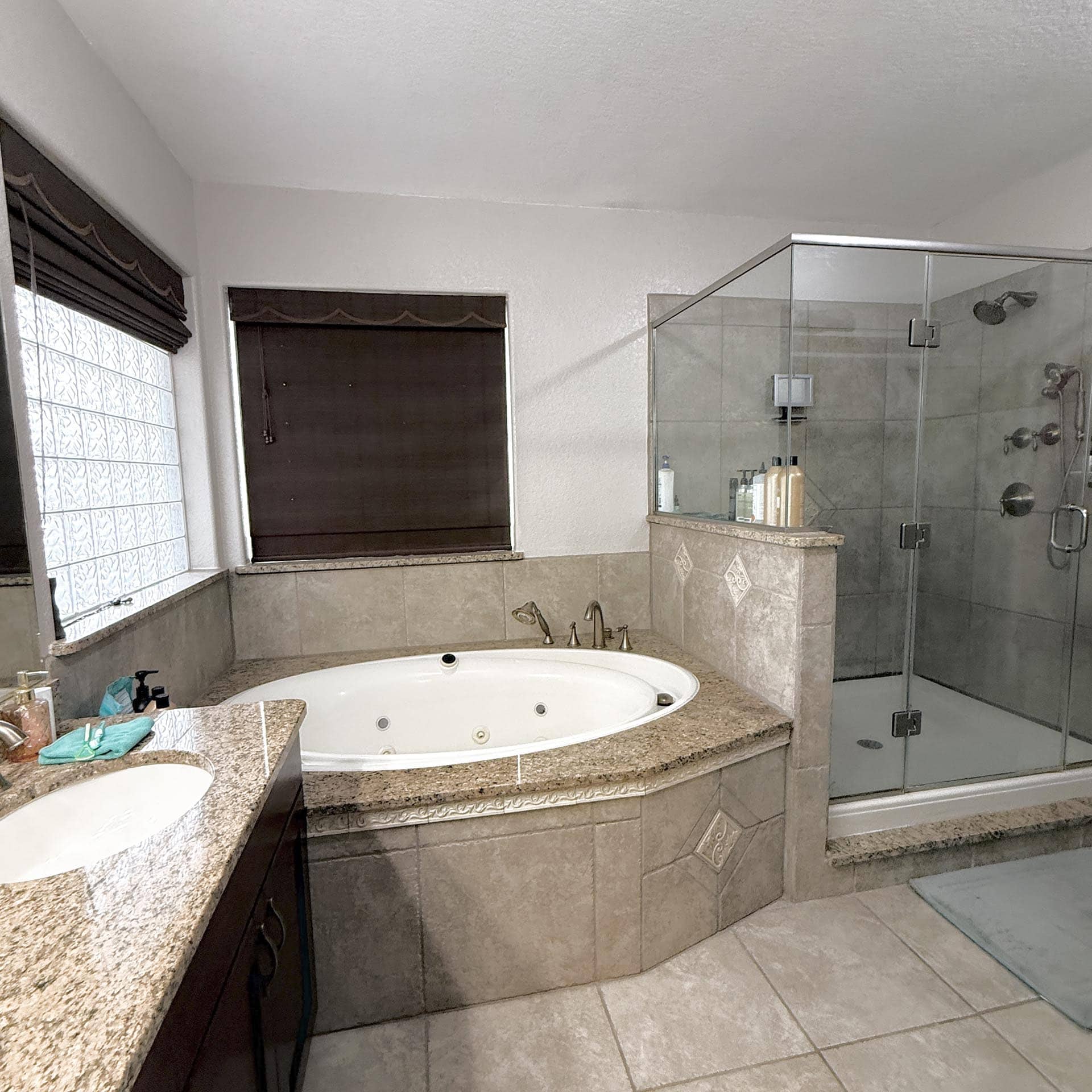 Modern bathroom with a circular whirlpool tub set in a granite surround, adjacent dark wood vanity on the left, and a glass-enclosed shower on the right.