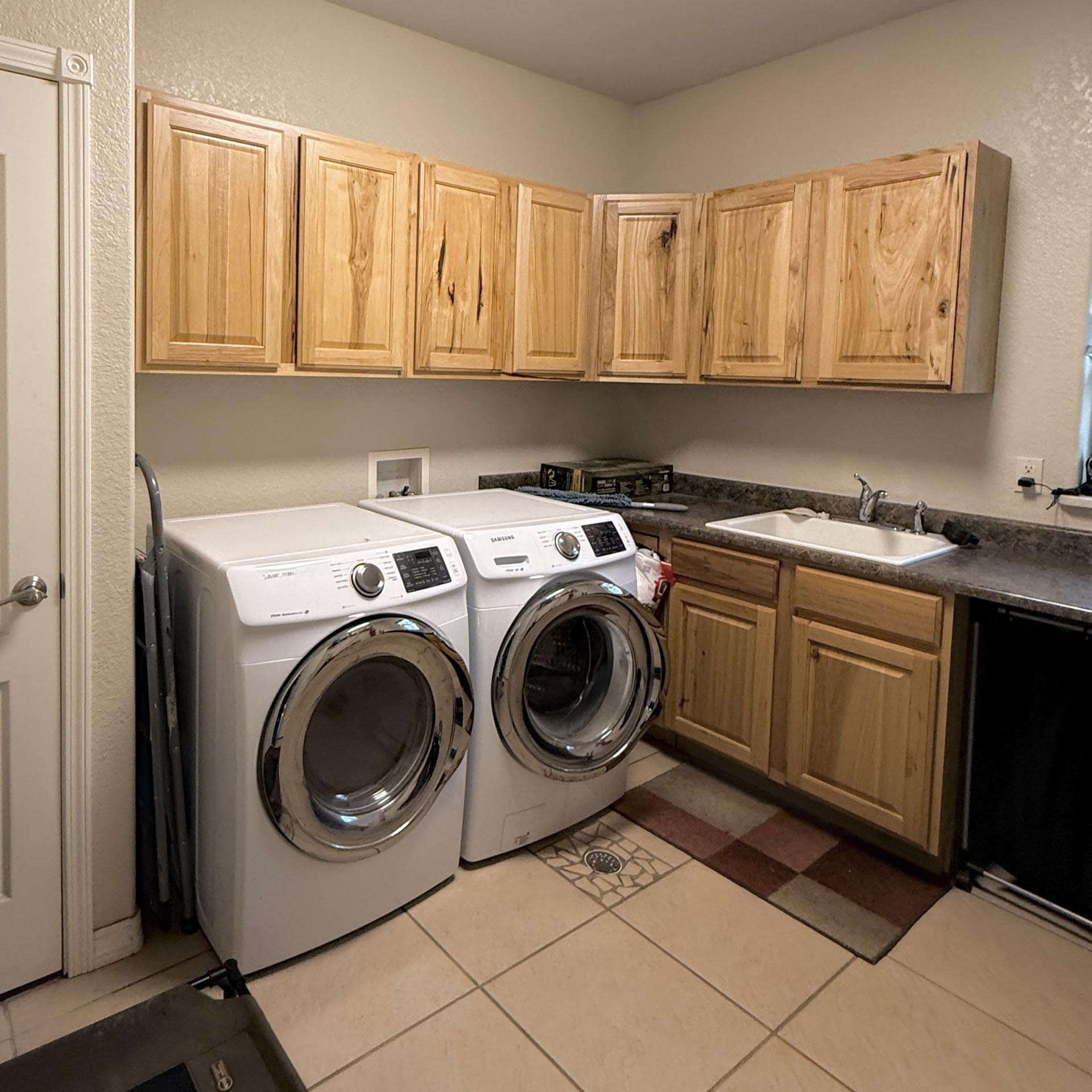 Laundry room with two front-loading washing machines under wooden cabinets and a sink to the right.
