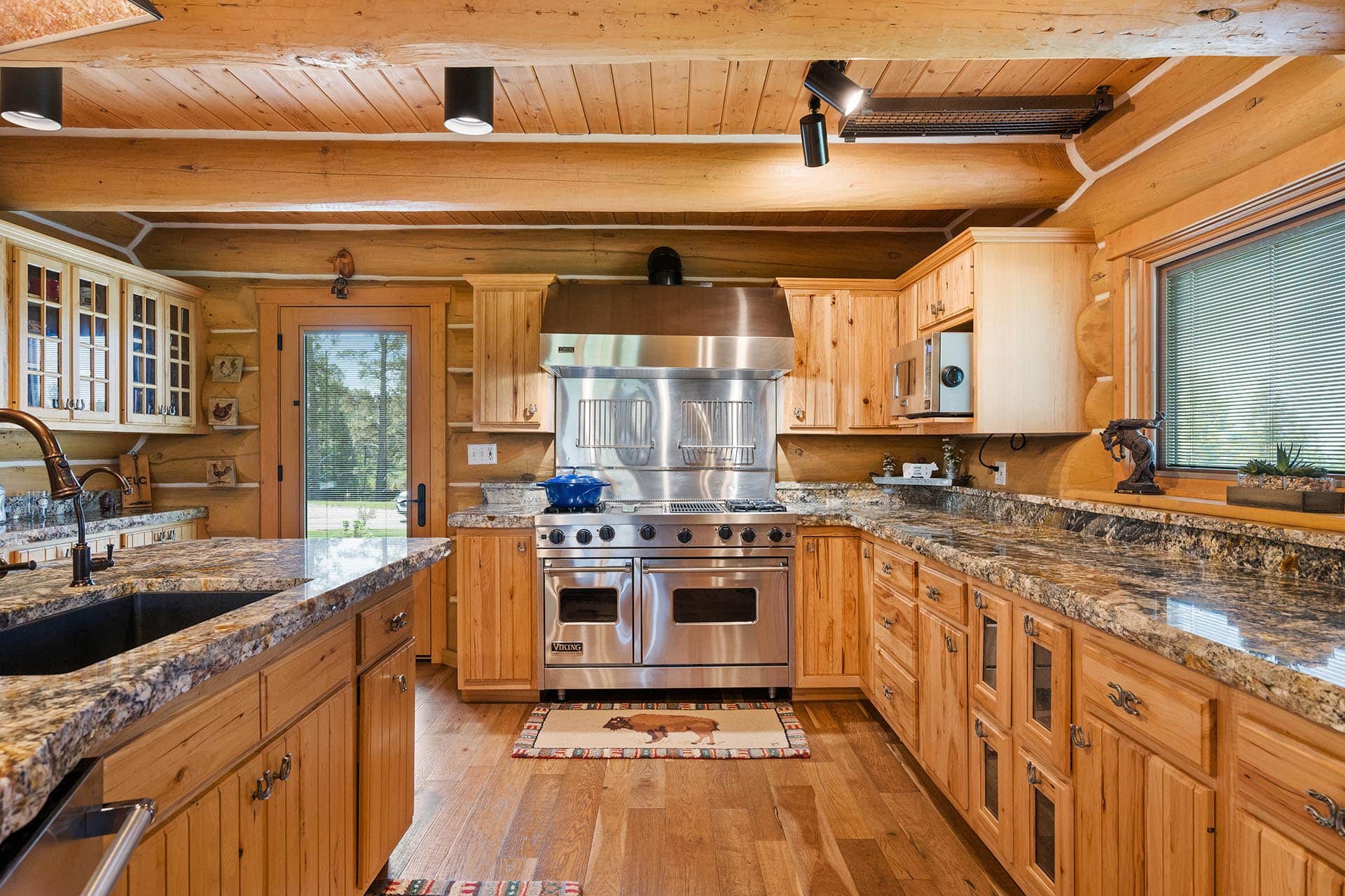 Rustic log cabin kitchen with a stainless Viking range, granite countertops, and wooden cabinets.