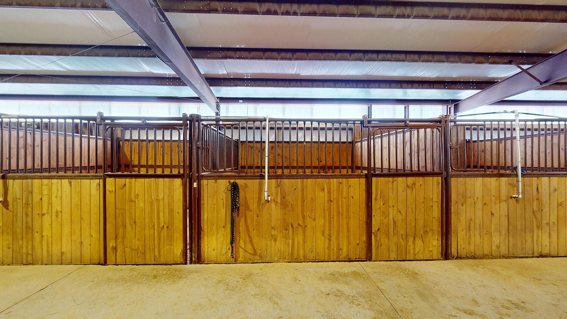 Interior of a horse stable: row of wooden stalls with metal railings, empty and tidy.