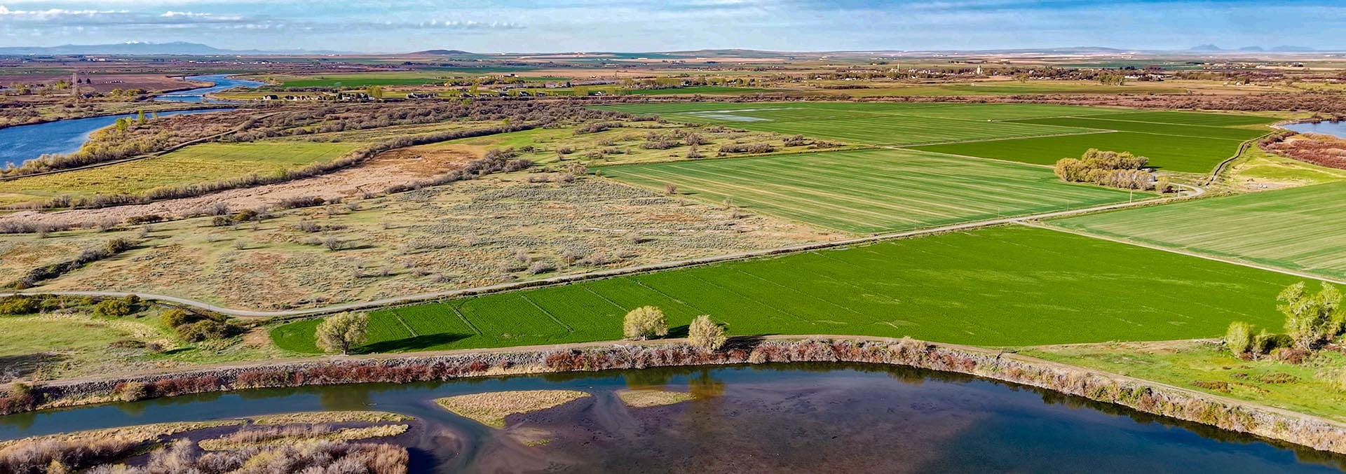 Aerial view of patchwork farmland with green fields, hedgerows, and a winding river in the foreground.