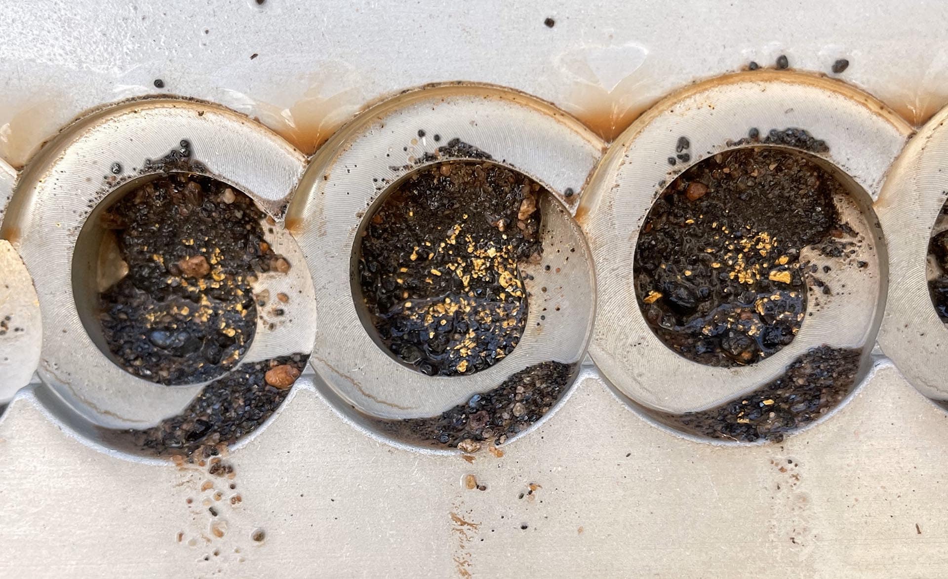Close-up of three engine combustion chambers showing heavy carbon buildup and soot inside each circular port.
