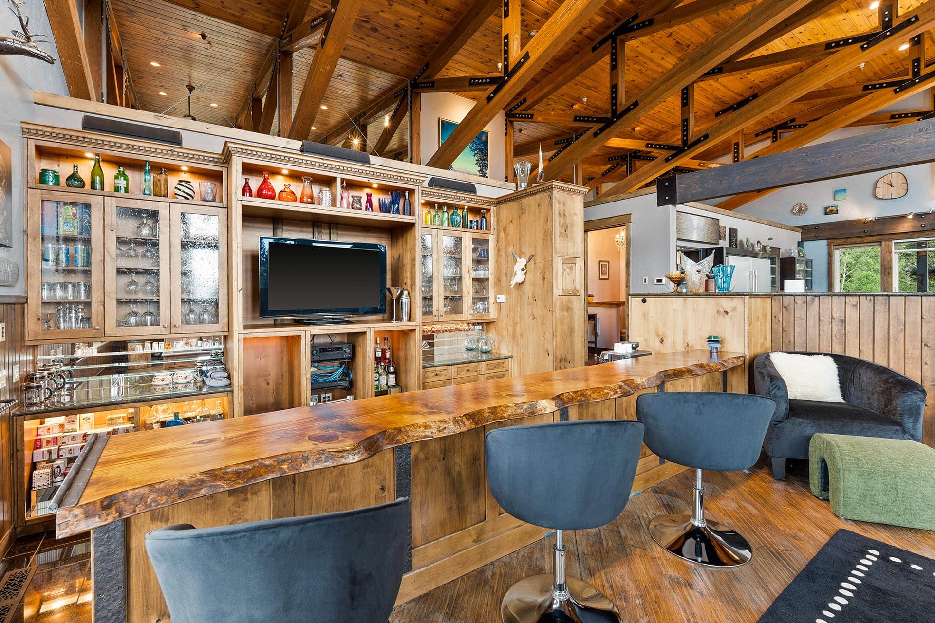 Wooden bar interior with a live-edge counter, glass cabinets, and colorful bottles on shelves