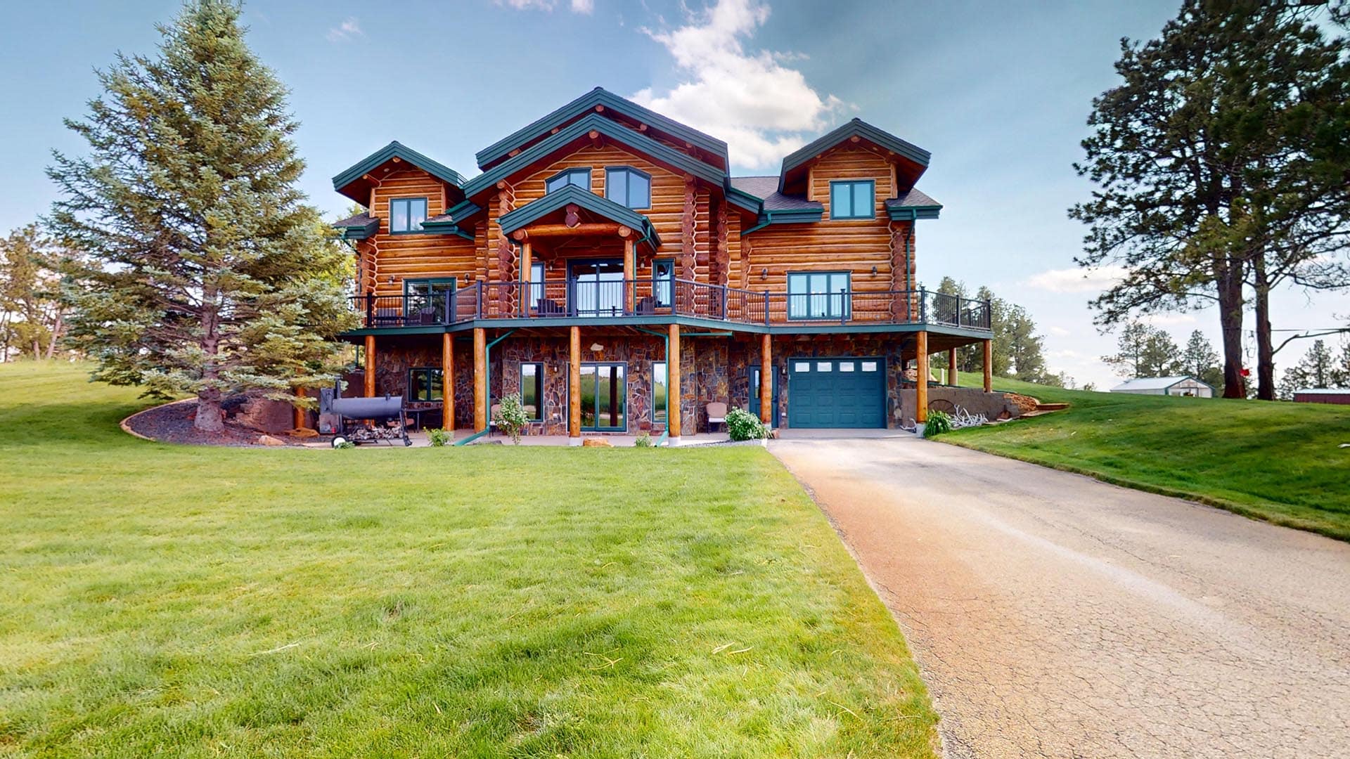 Large log cabin-style house on a grassy lawn with a curved driveway and a two-car garage.