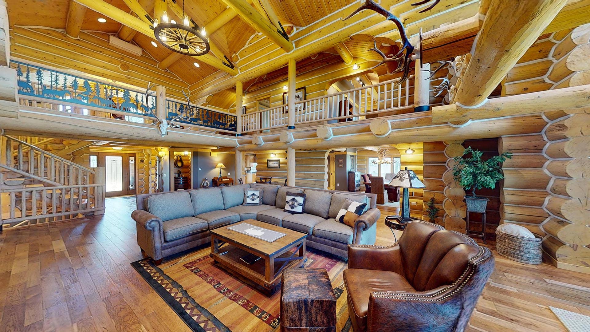 Open log-cabin living room with a gray sectional, leather chairs, and a wooden coffee table under exposed timber beams.