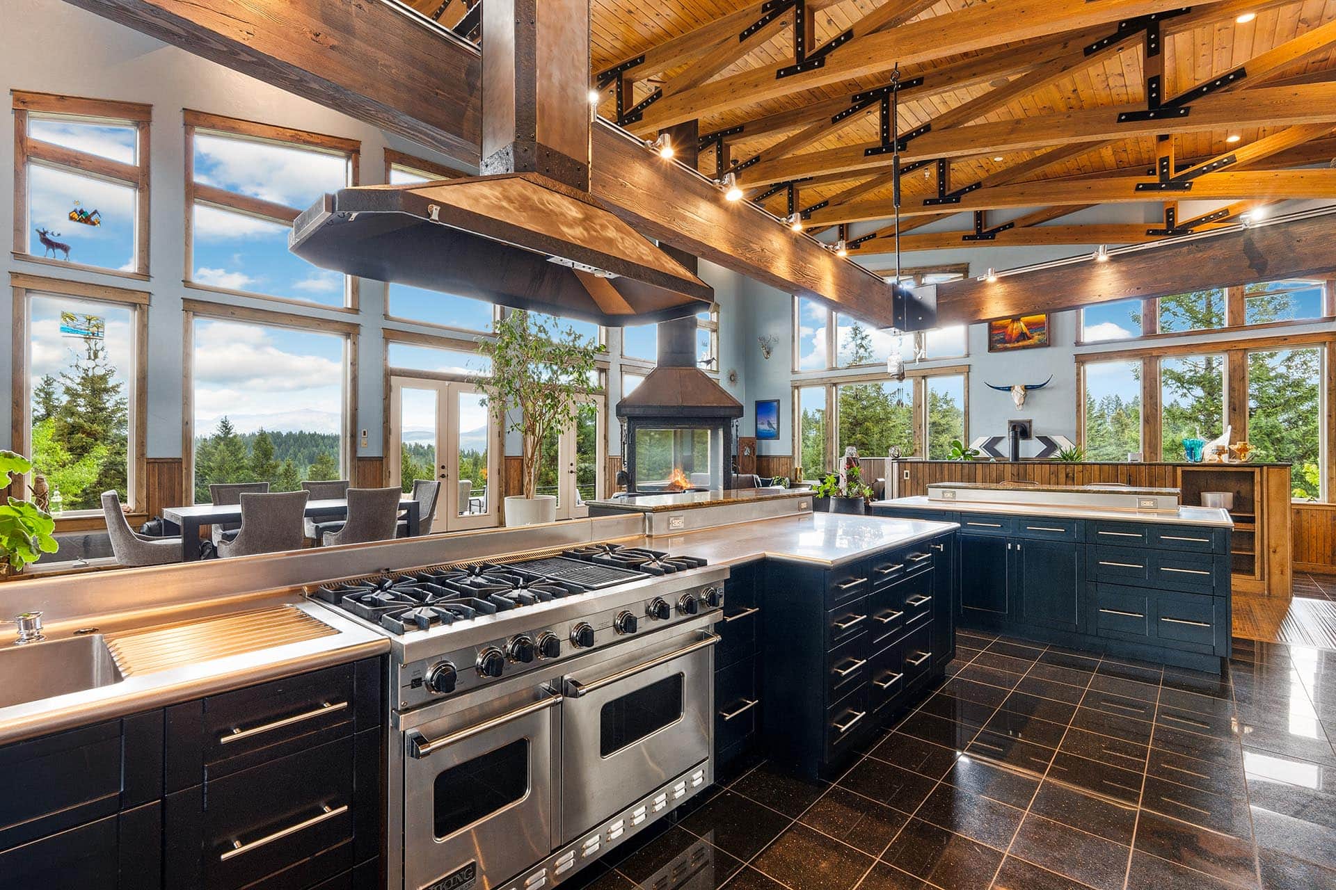 Spacious kitchen with black cabinets, stainless steel six-burner range, and a central island under exposed wooden beams.
