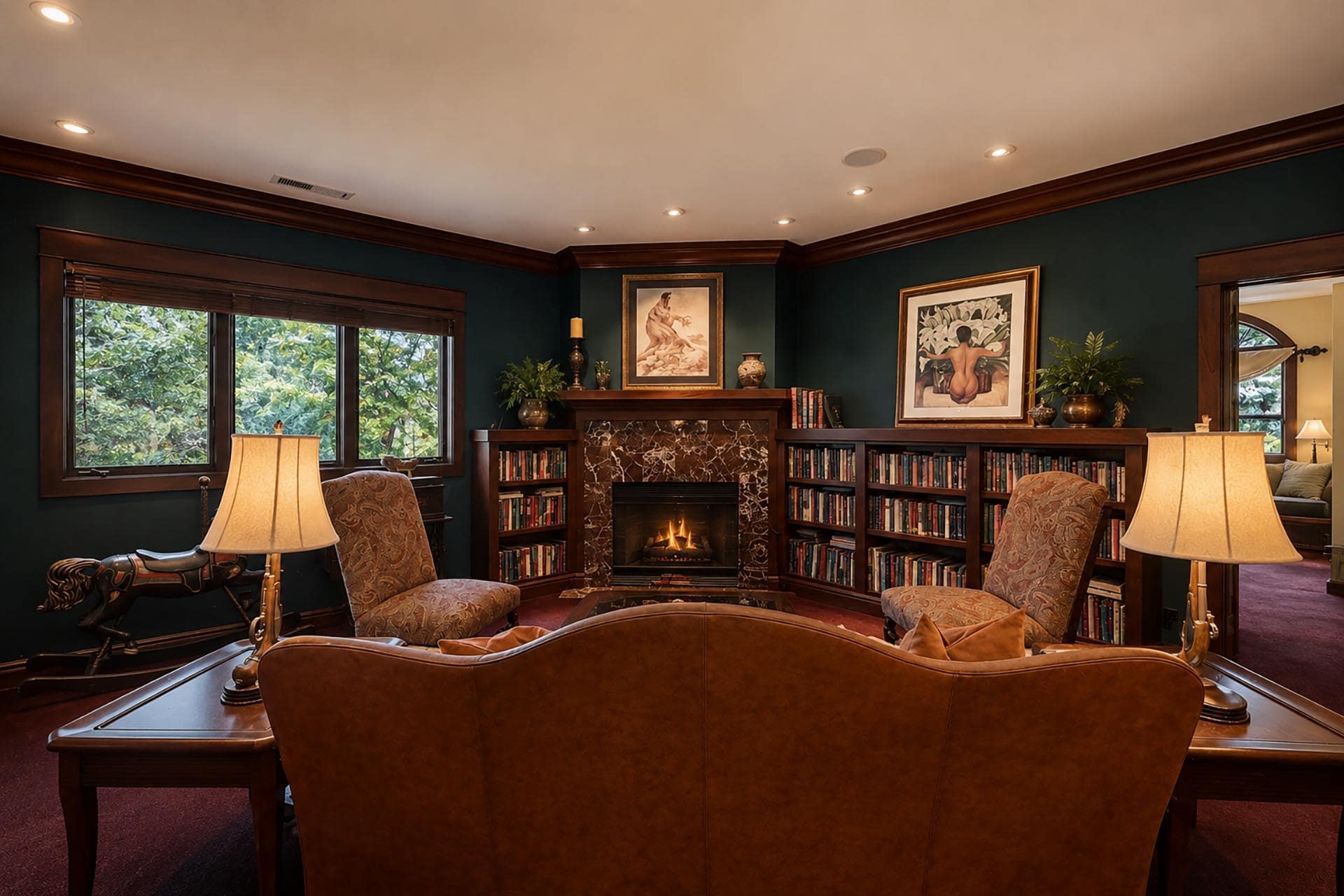 Cozy library-style living room with a marble fireplace, dark wood bookshelves, framed art, and upholstered seating.