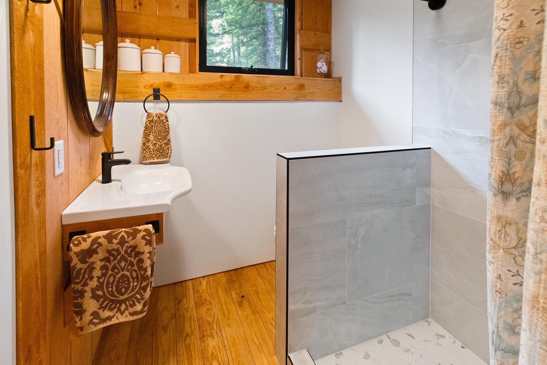 Rustic bathroom with a white sink, black faucet, wood paneling, and a patterned towel hanging from a ring near a windowed ledge and jars on the sill.