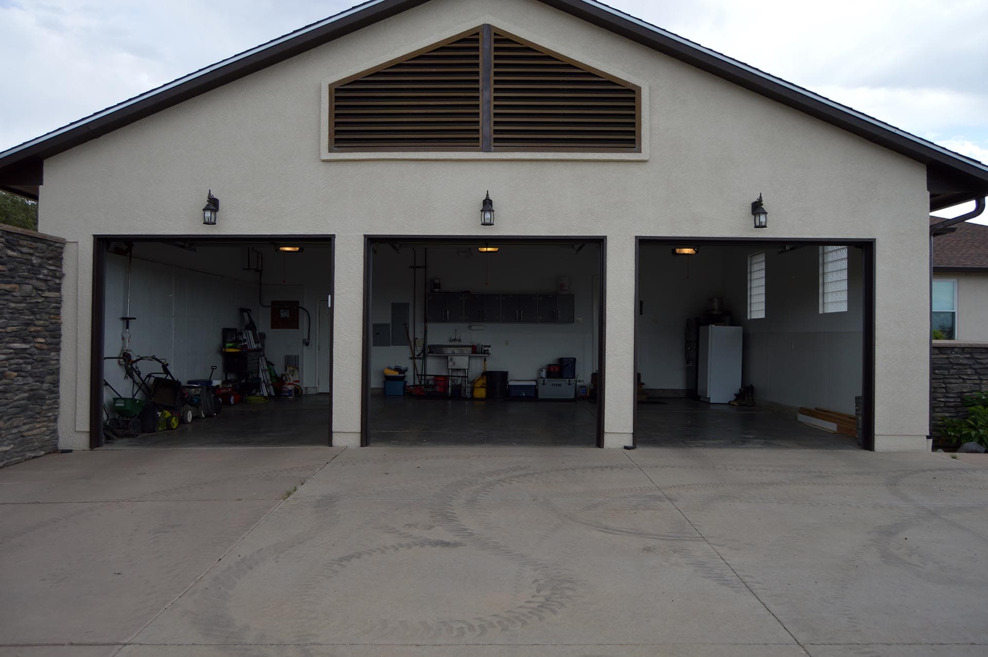 Three-car garage with open doors; cluttered workshop with tools and cabinets inside.
