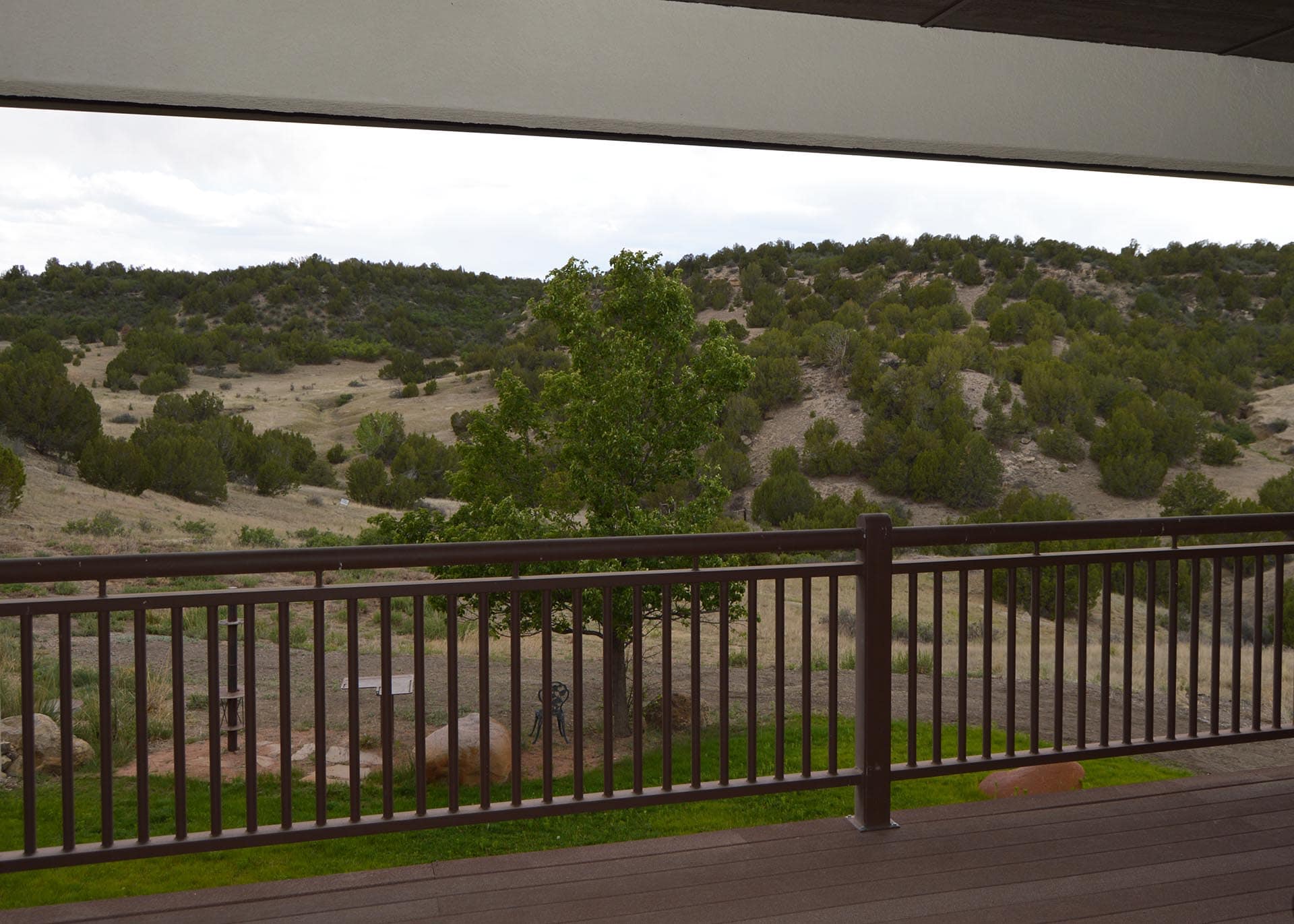 Balcony railing in the foreground with a hillside of trees and shrubs and a cloudy sky in the background.