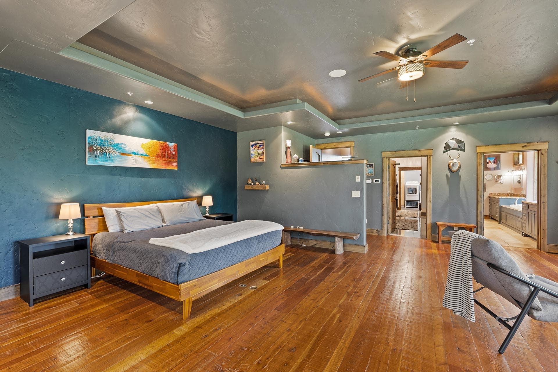 Spacious bedroom with blue walls, wooden floor, and a platform bed flanked by nightstands beneath a ceiling fan.