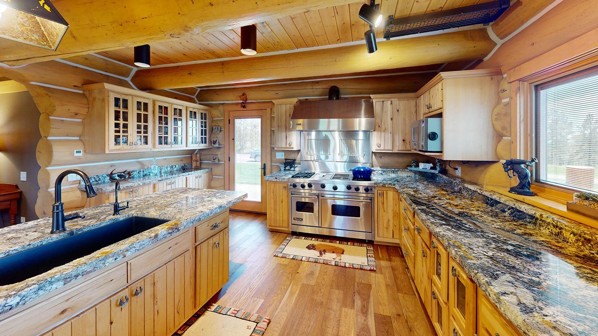 Rustic log-cabin kitchen with granite countertops, island sink, and a large stainless steel stove.