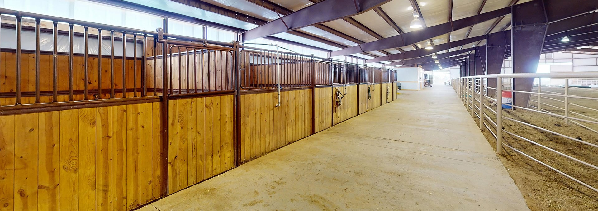 Spacious indoor horse stable with wooden stalls and metal fencing.