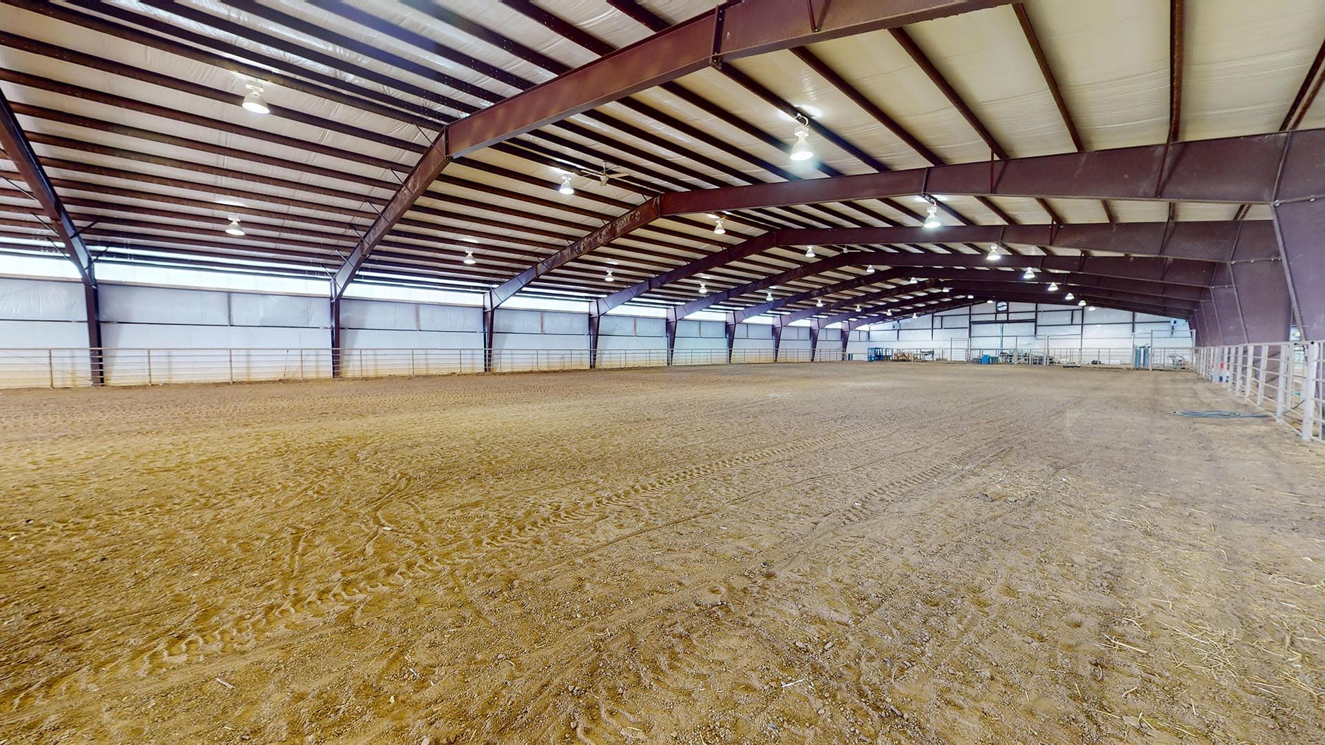 Interior of a large indoor riding arena with a dirt floor and metal support beams