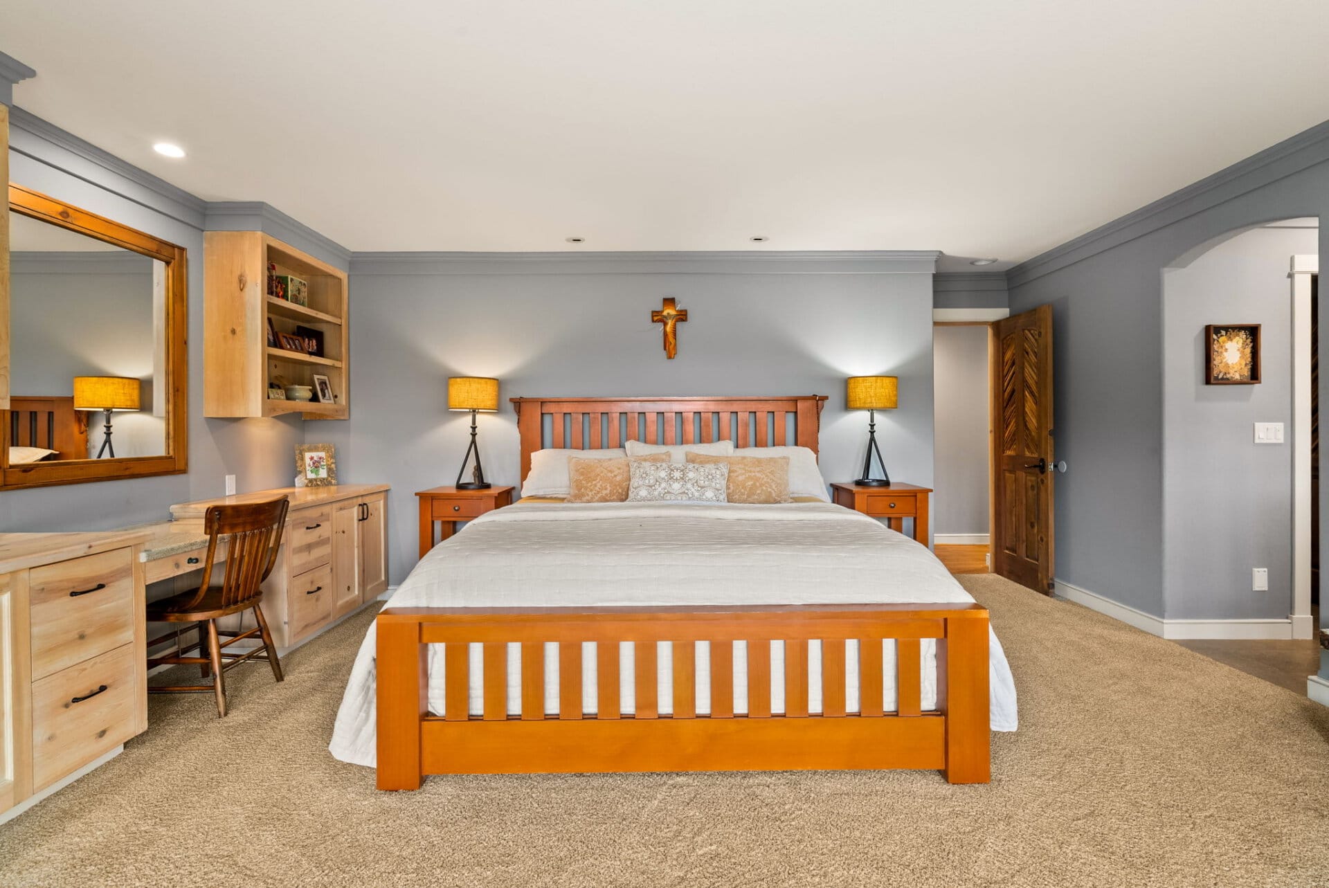 Bedroom with a wooden bed, blue-gray walls, two nightstands with lamps, and a crucifix above the headboard.