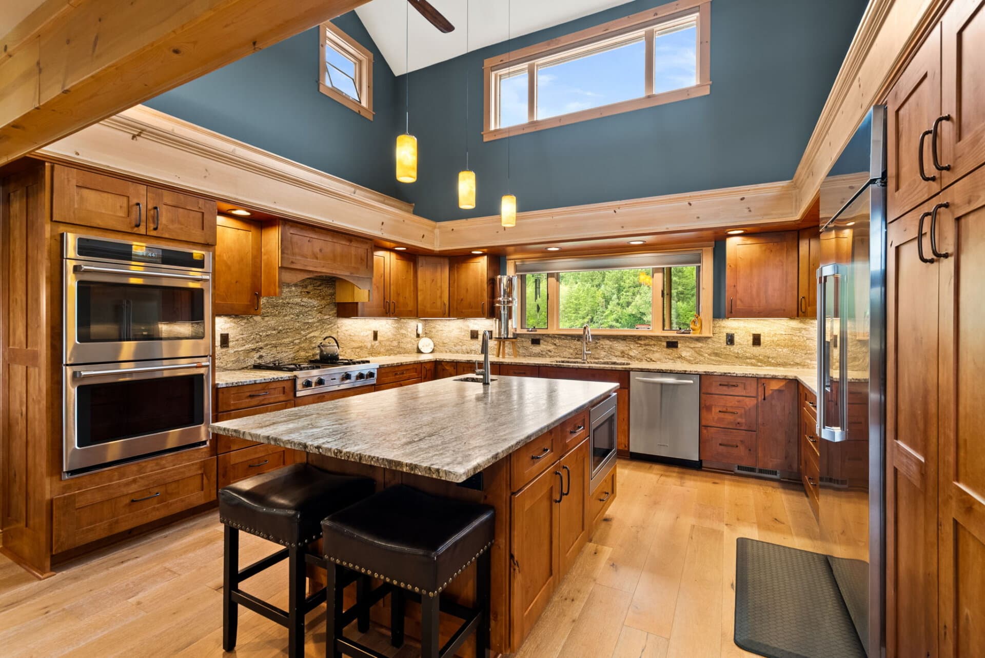 Modern rustic kitchen with granite island, warm wood cabinetry, and stainless appliances under blue walls.