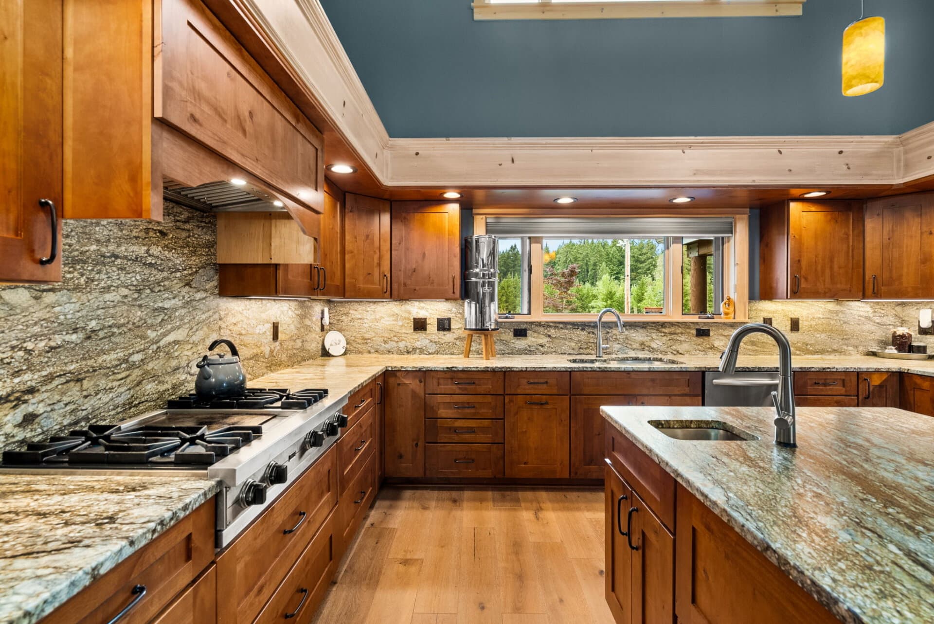 Kitchen with warm wood cabinets, granite countertops, and a central island; view of outdoors through a large window above the sink.