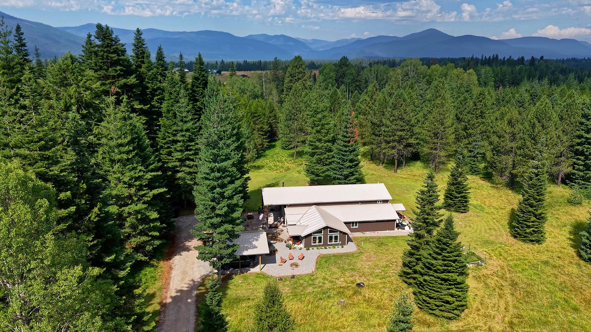A cabin-style house with a patio surrounded by a pine forest and distant mountain range on the horizon.